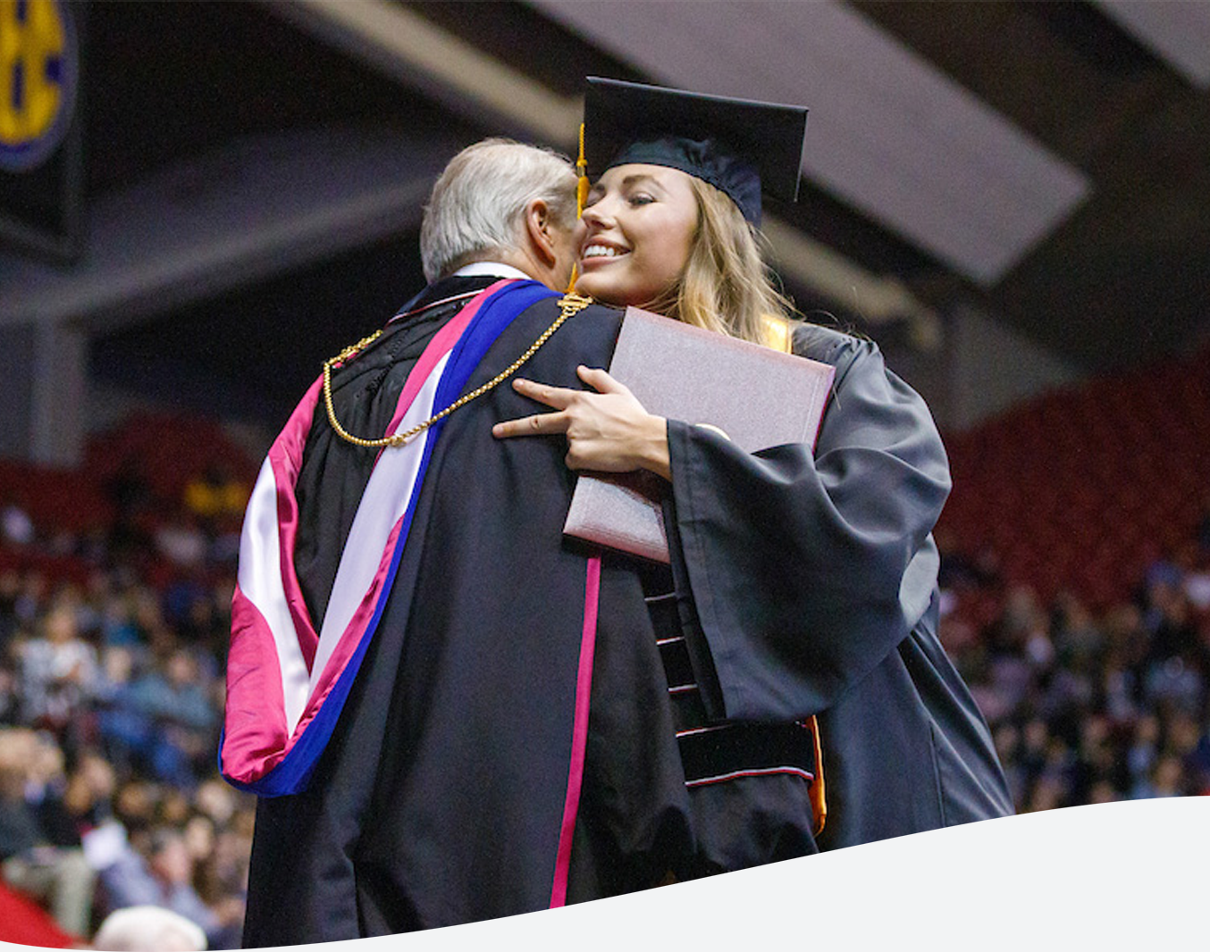 Graduate hugging UA President Dr. Bell on-stage at commencement ceremony