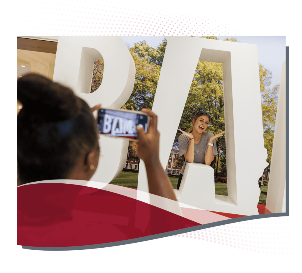 Student taking a picture behind a large cutout of the word "Bama"